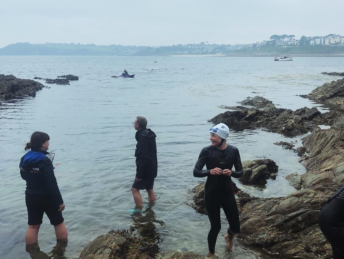 Swimmer exits the water smiling after a long swim event, moody sky and sea behind them