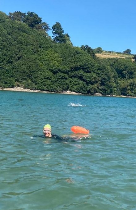 open water swimmer looks towards camera smiling, summers day, river swim turquoise waters.