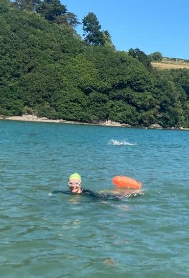 open water swimmer looks towards camera smiling, summers day, river swim turquoise waters.